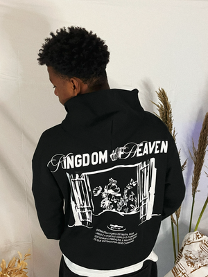 Model wearing oversized black hoodie with 'KINGDOM OF HEAVEN' graphic, featuring ribbed hem and cuffs.