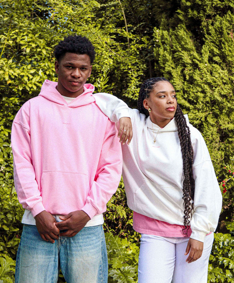 Two models wearing oversized pink and white sweatshirts in a garden setting, showcasing casual streetwear style.